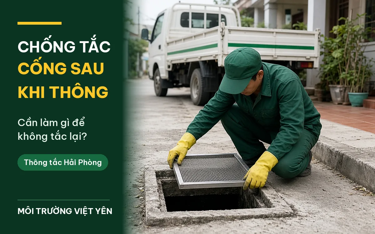 Kỹ thuật viên mặc đồng phục xanh lá đậm, đội mũ lưỡi trai, đeo găng tay vàng quỳ bên hố ga bê tông mở nắp trong ngõ, đang lắp tấm lưới inox chắn rác lên miệng hố, phía sau là xe tải trắng sọc xanh, ảnh bìa bài chống tắc cống sau khi thông